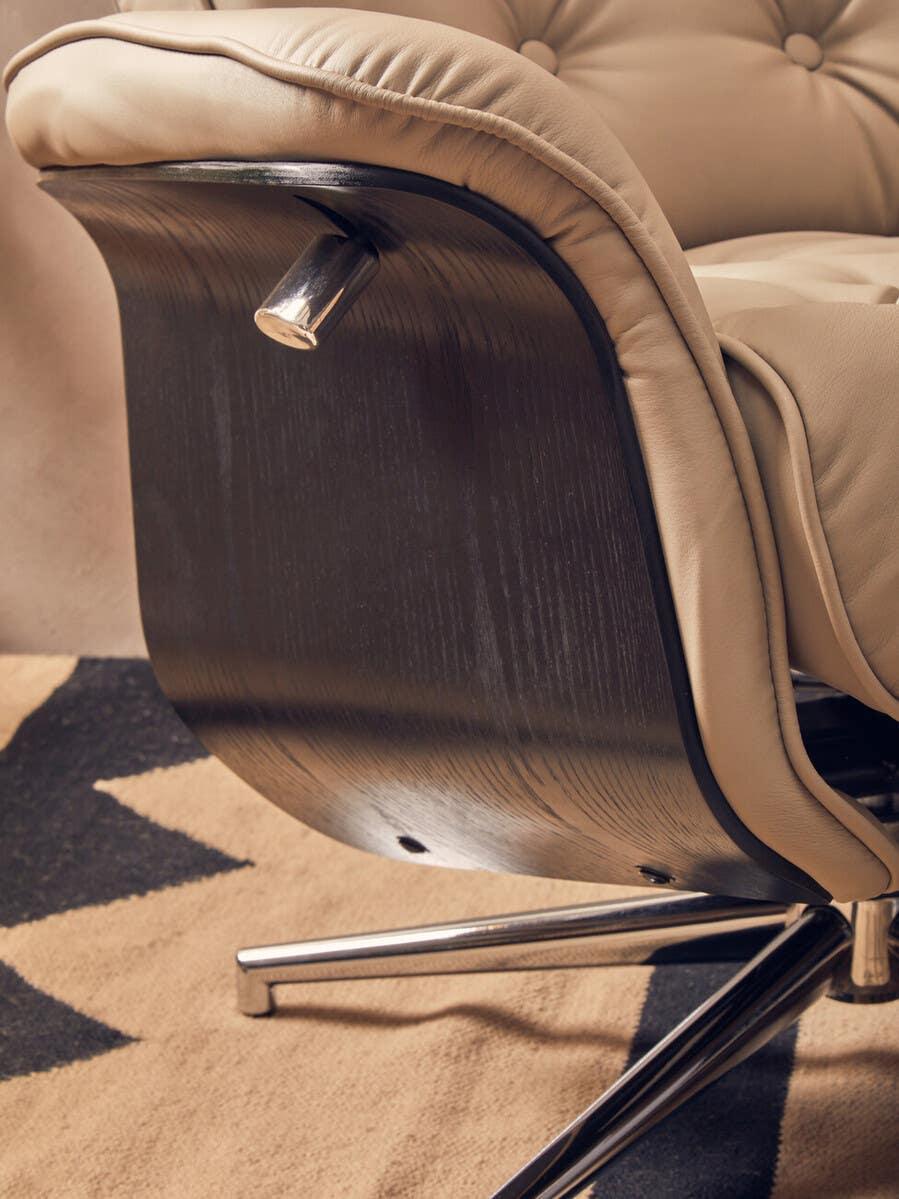 Beige leather armchair with curved wood back and chrome swivel base on patterned rug