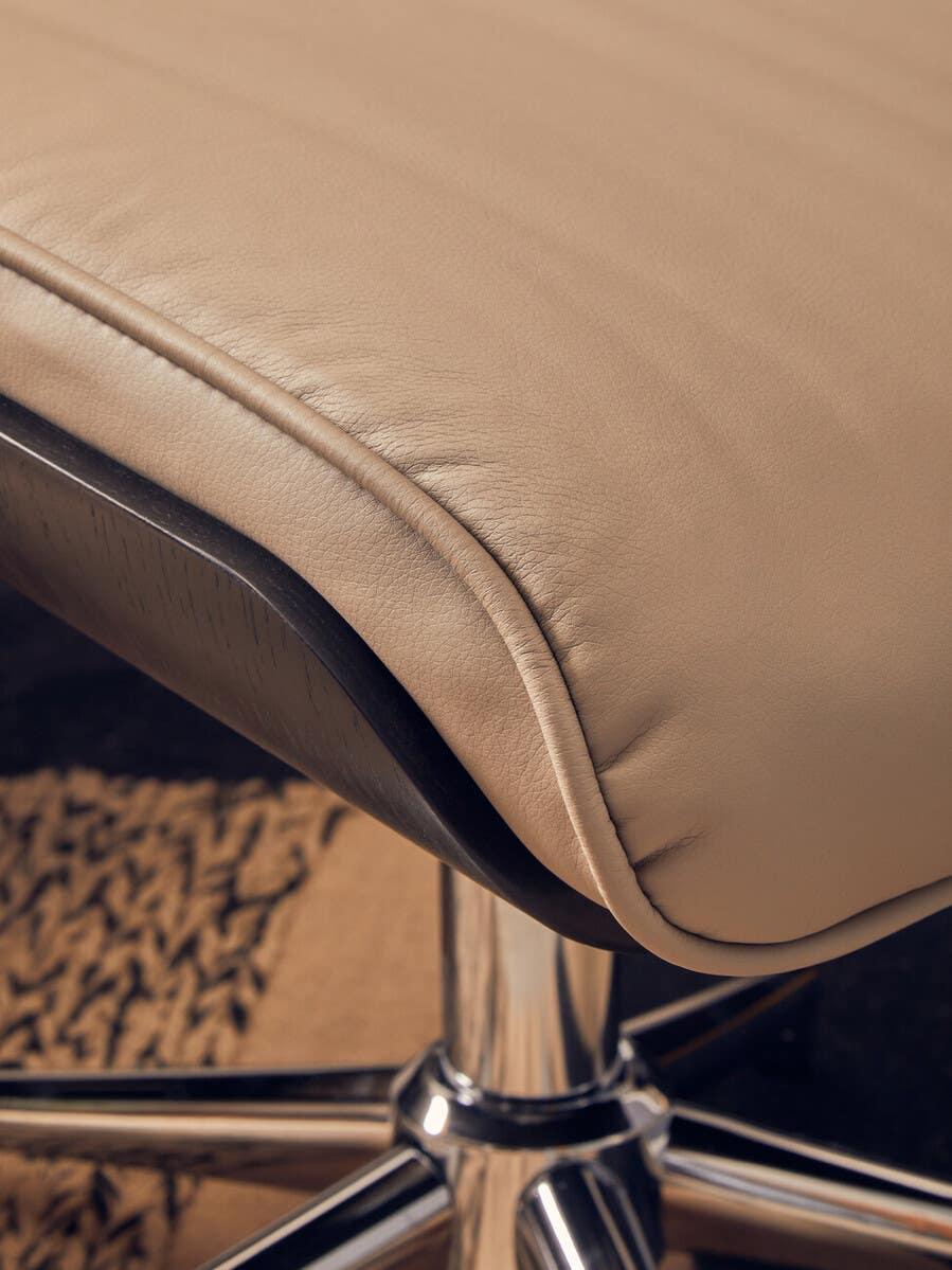 Closeup of beige leather chair seat with chrome legs on patterned rug