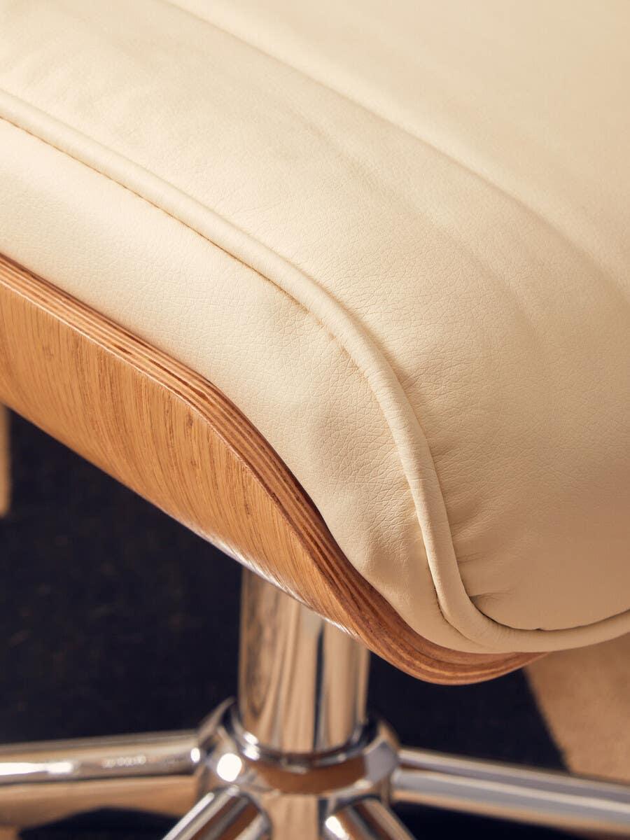 Cream leather bar stool with curved wooden edge and chrome base, close-up seat view