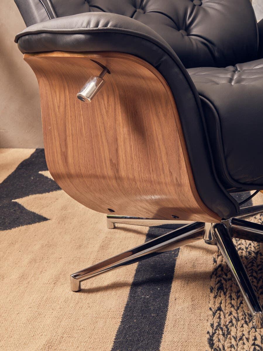 Black leather recliner chair with curved wood backrest and metal swivel base on patterned rug