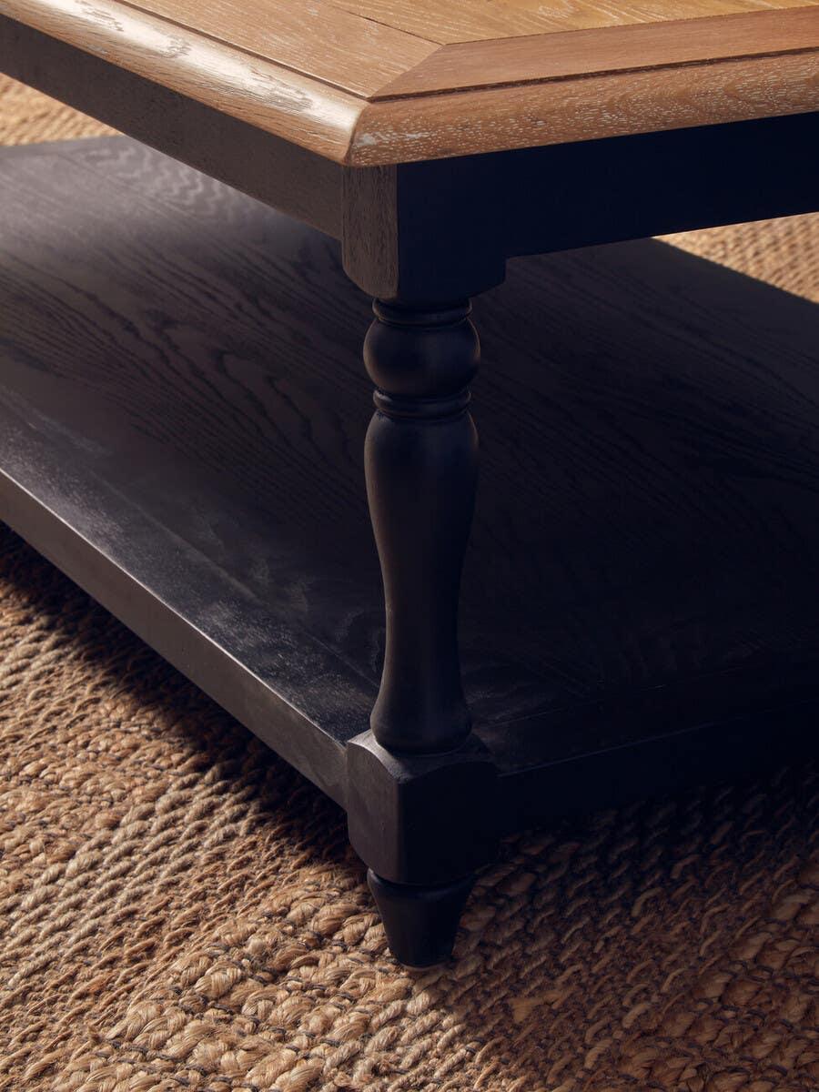 Wood coffee table with turned black legs and lower shelf on woven rug