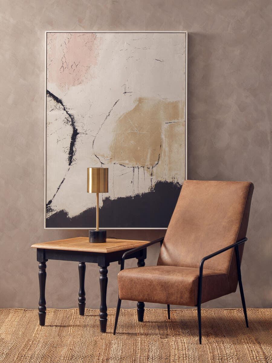 Brown leather accent chair with black metal arms beside wooden side table and gold table lamp