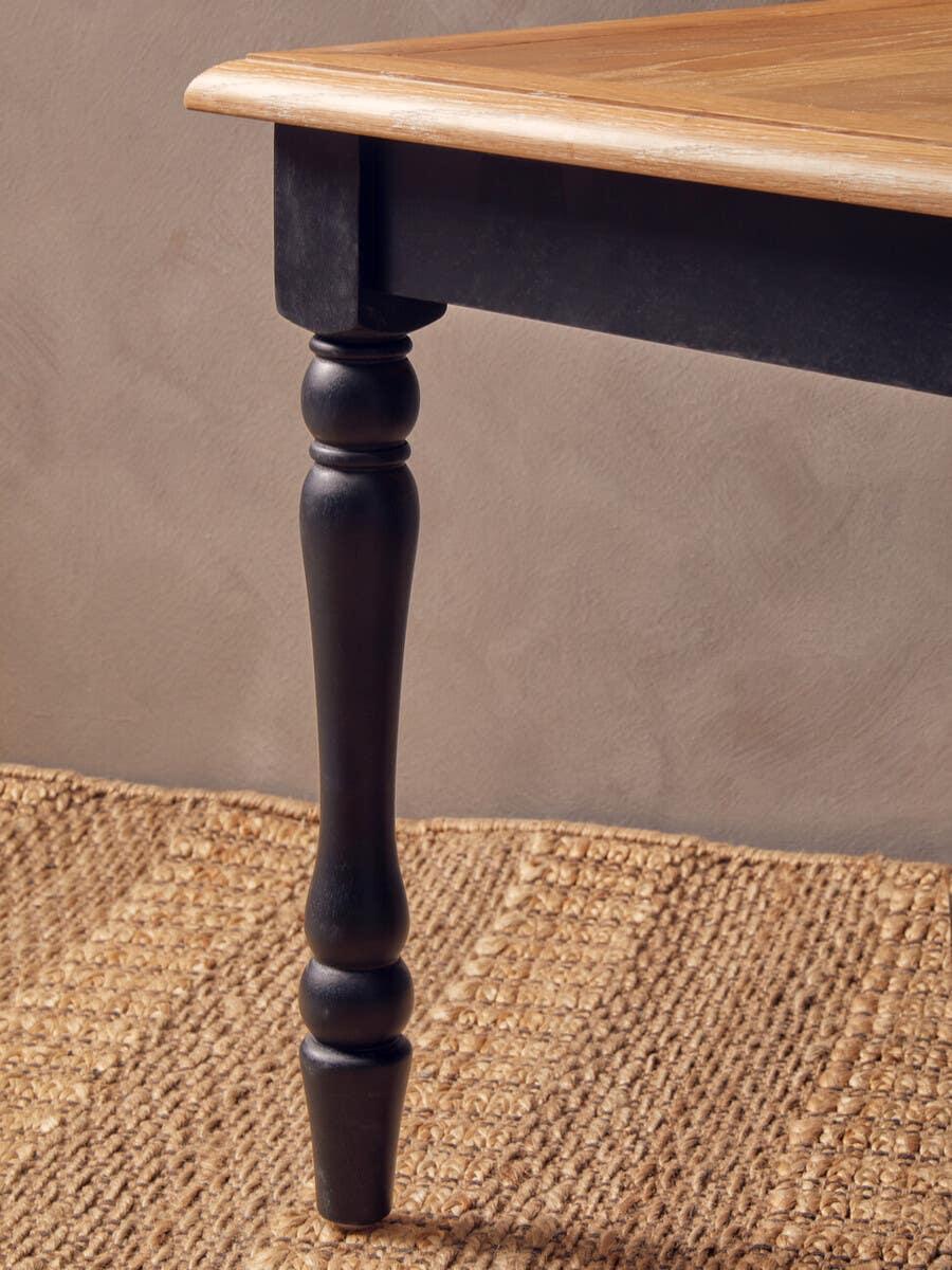 Oak dining table corner with turned black wood leg on woven rug