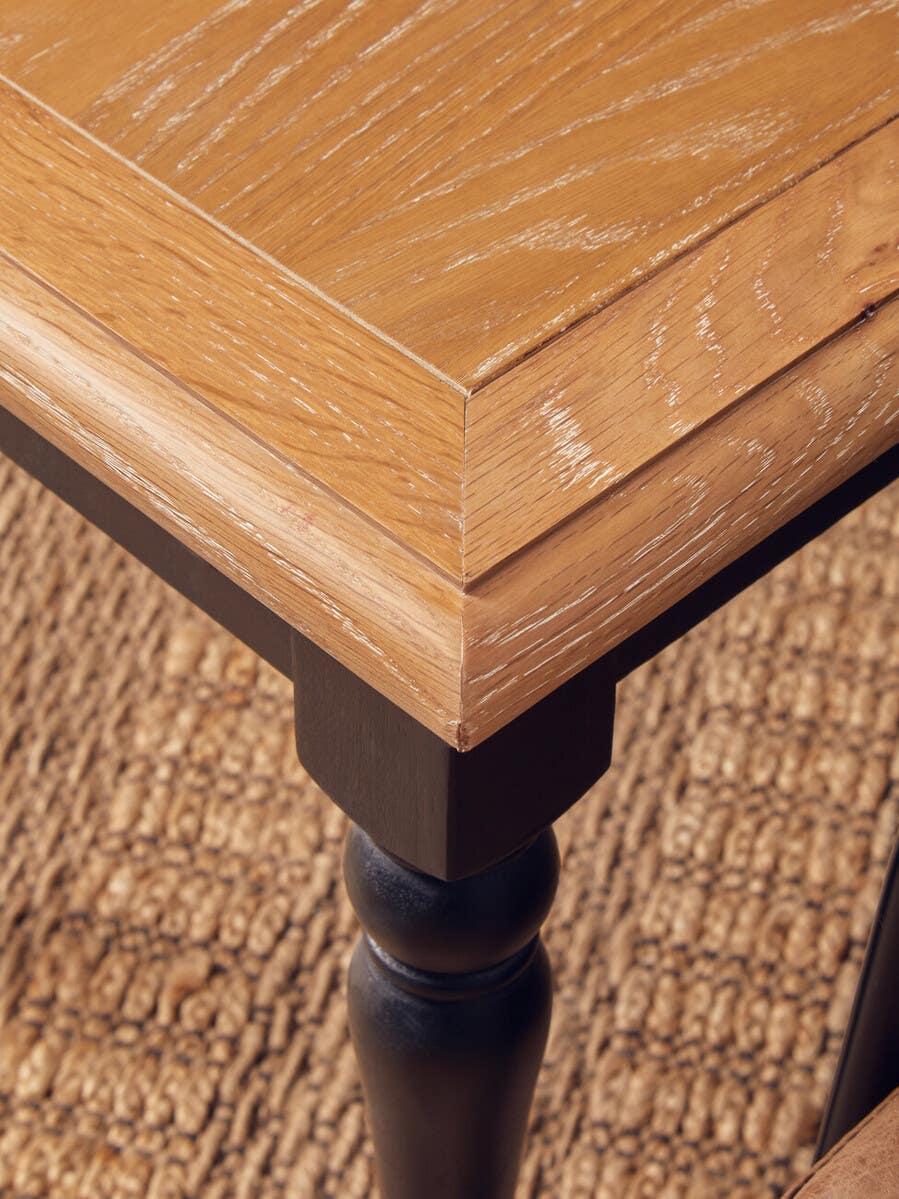 Closeup of oak dining table corner with black turned leg on woven rug