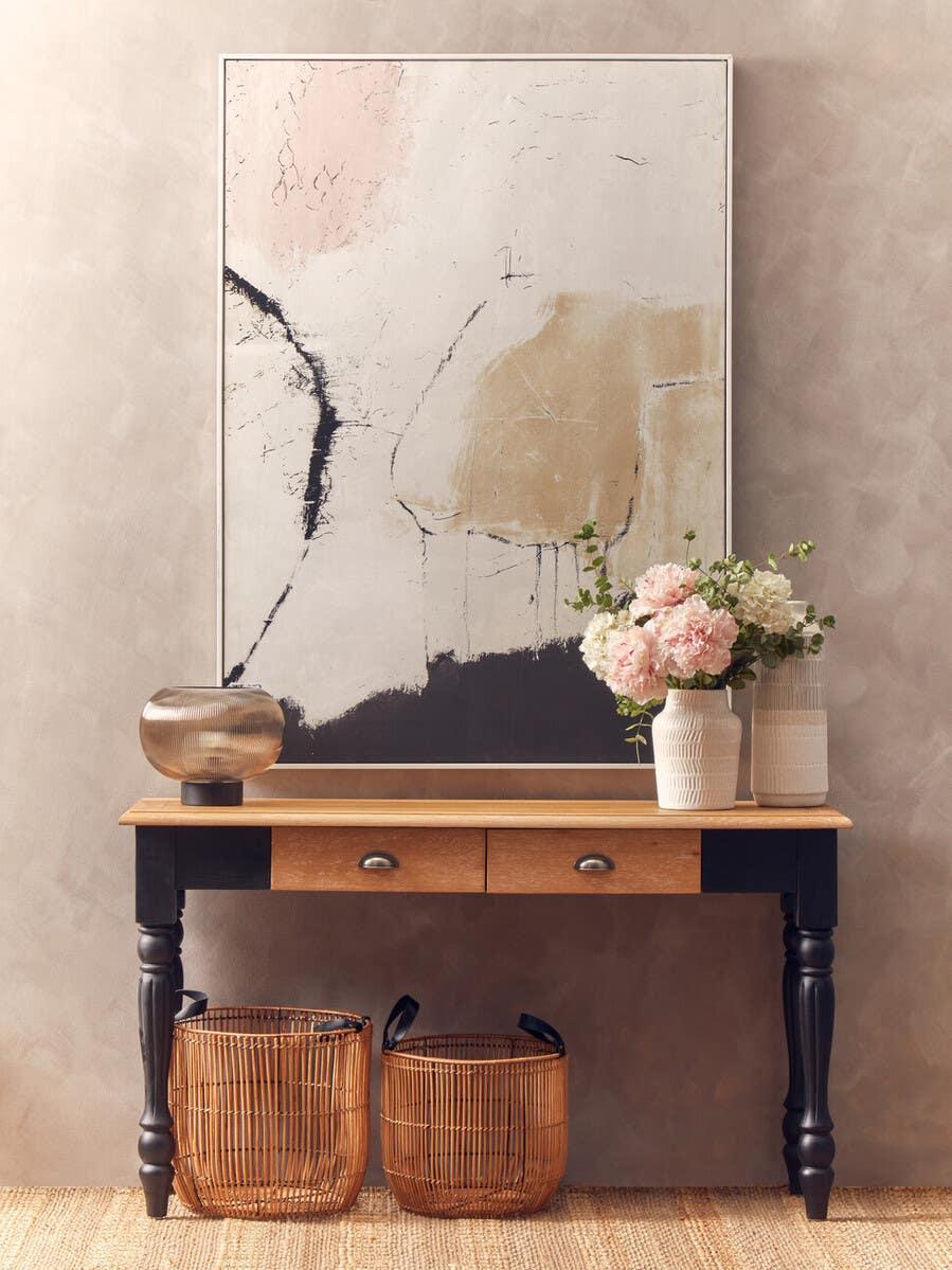 Wood console table with black legs, two drawers, baskets, and decorative vases in hallway