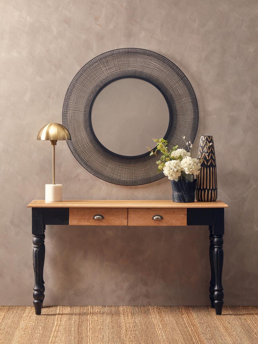 Wood console table with black legs, brass lamp, round wall mirror, vase and flowers