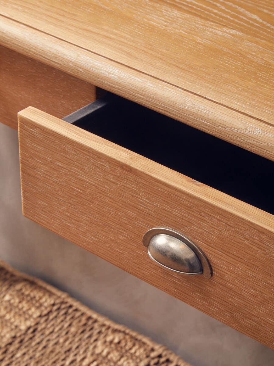 Oak wood drawer with metal cup handle partially open above woven rug