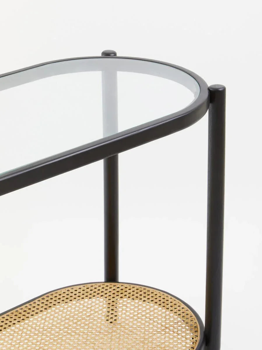 Glass top side table with black metal frame and woven rattan shelf, close-up angle
