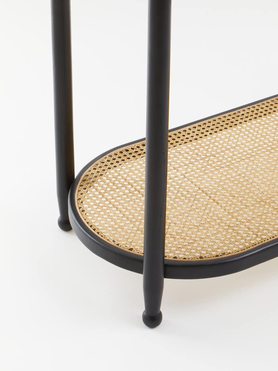 Black metal side table with lower rattan shelf and rounded legs on white background
