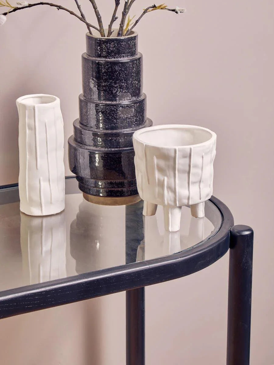Modern ceramic vases and white planter on glass console table against pastel wall