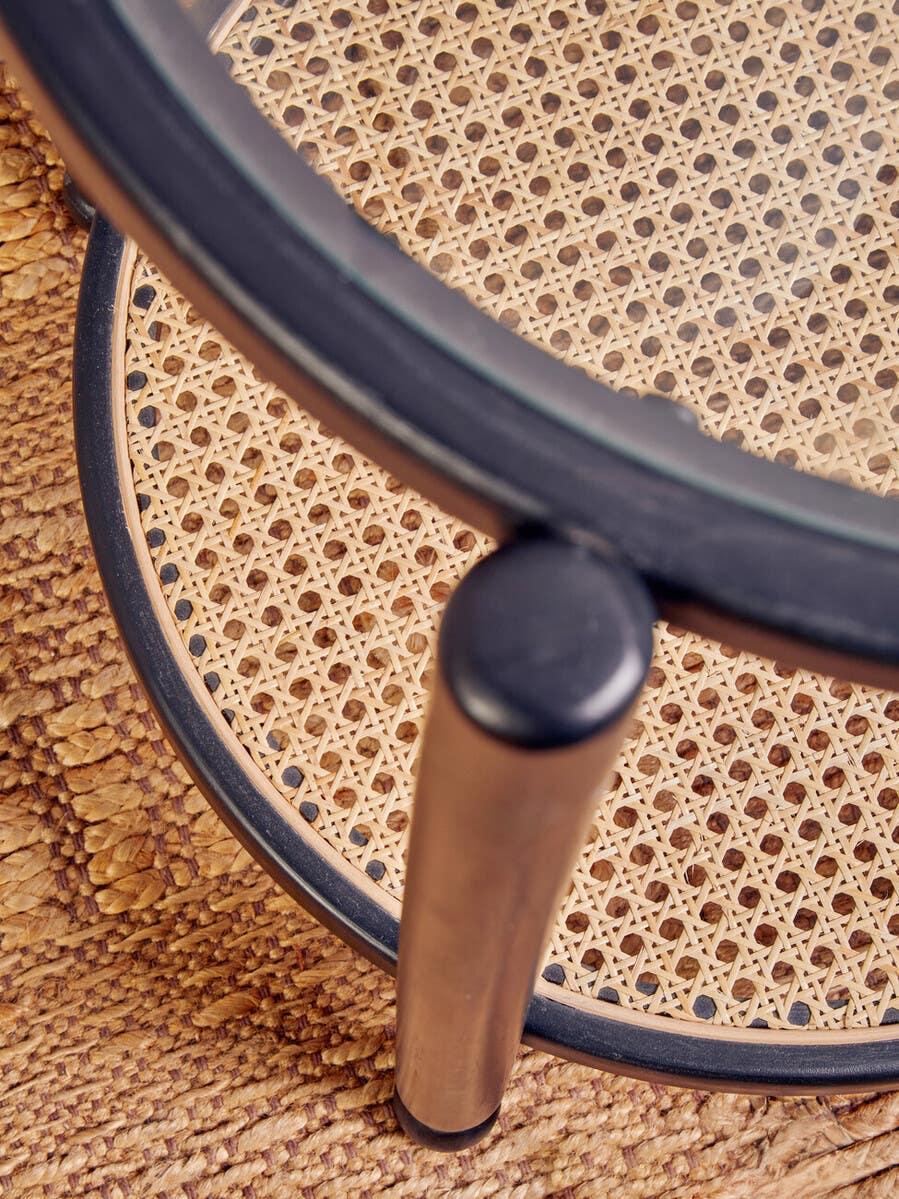 Round rattan side table with glass top and metal legs on woven rug
