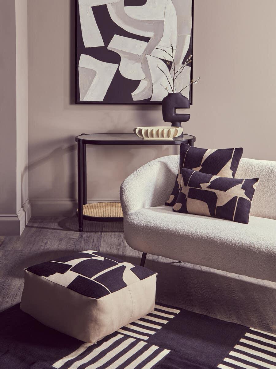Modern living room with cream sofa, black and cream cushions, patterned pouffe and console table