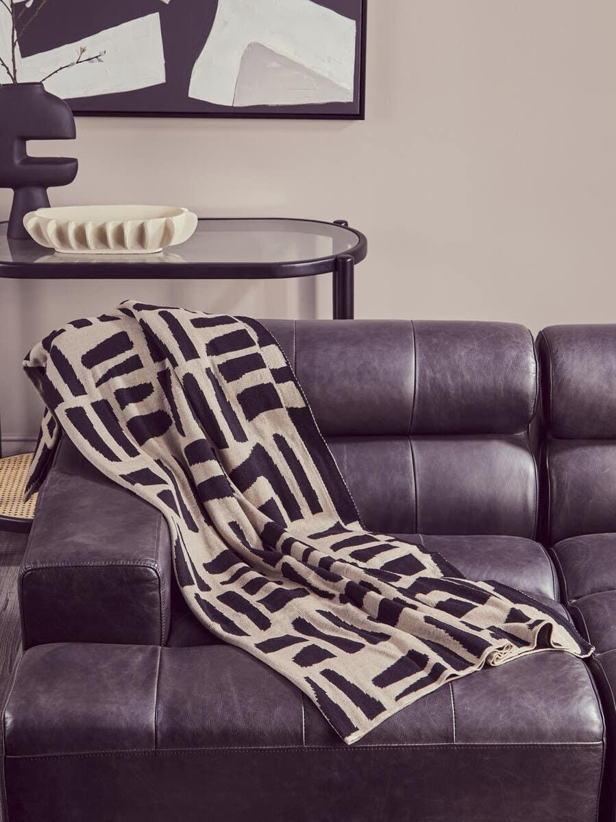 Black and beige geometric throw blanket on dark leather sofa in modern living room