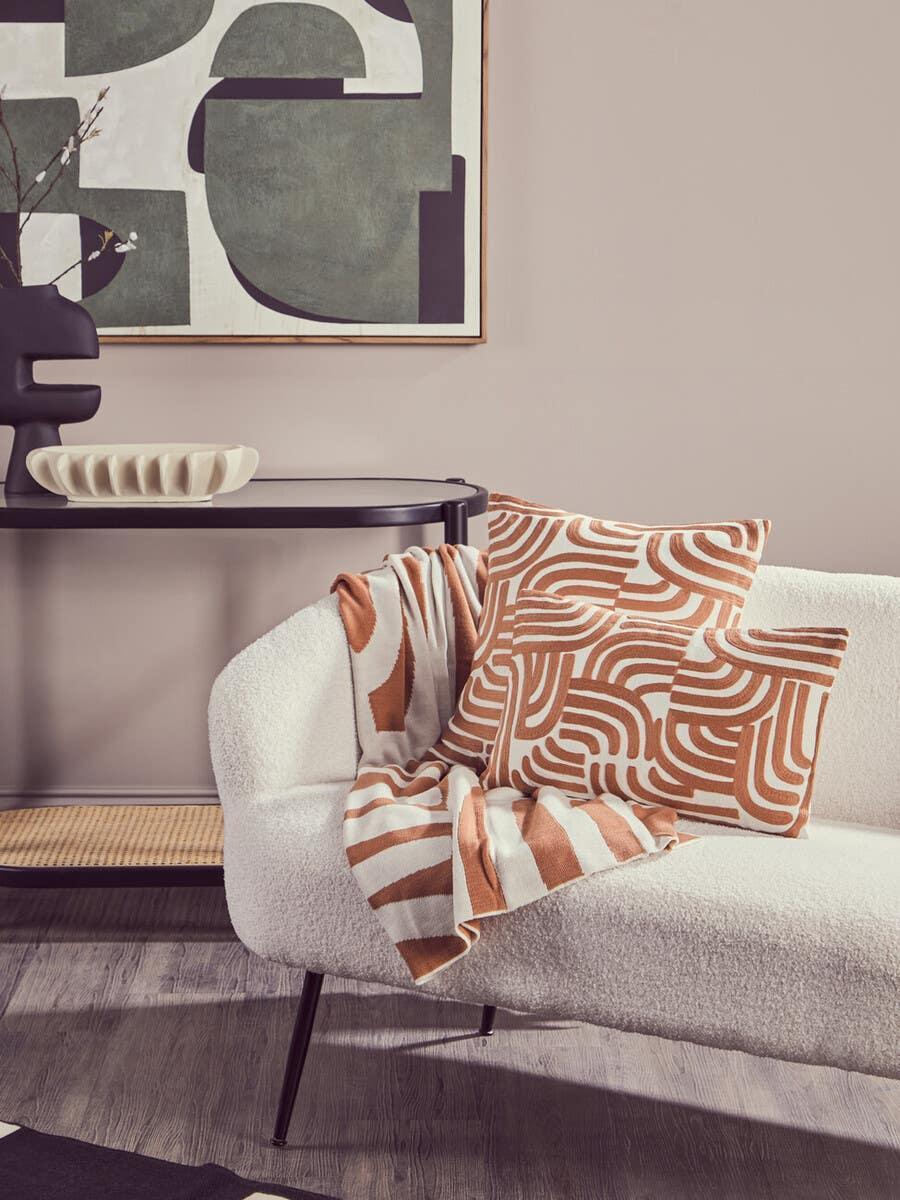 Bouclé sofa with terracotta geometric cushions and throw in modern living room setting