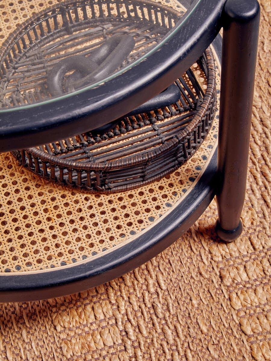 Round rattan side table with black frame and glass top on woven rug