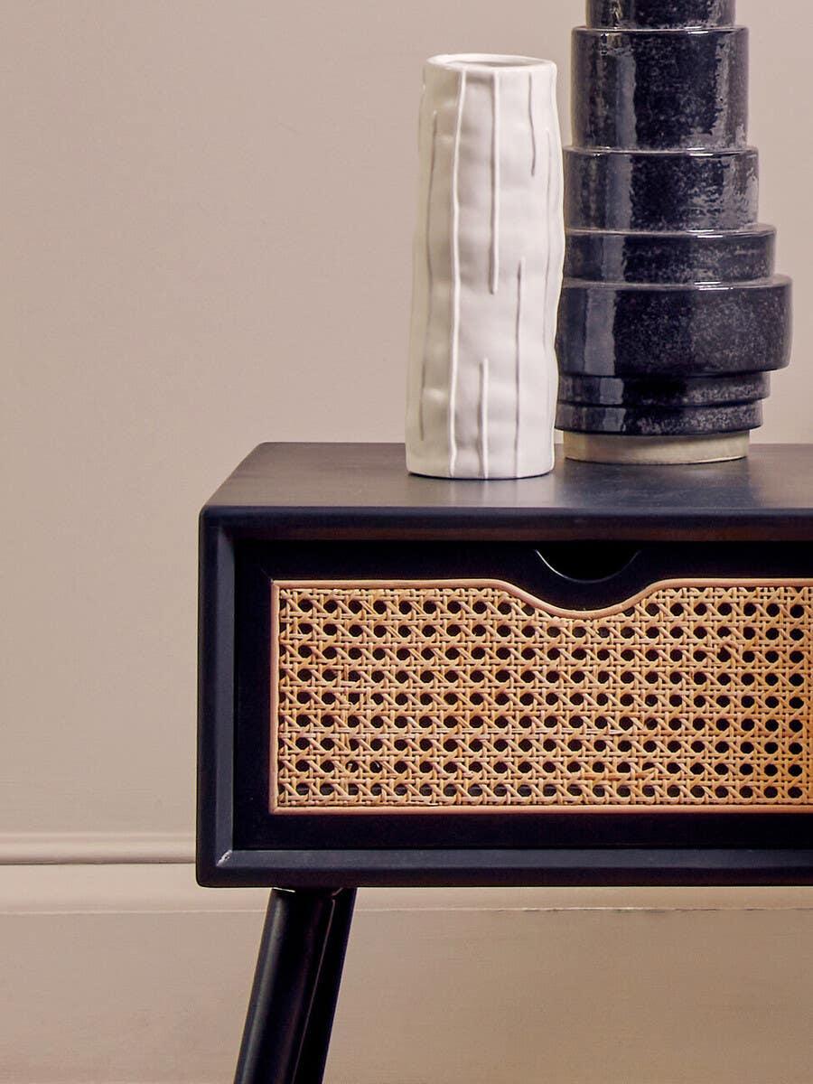 Black bedside table with woven rattan drawer and ceramic vases on top