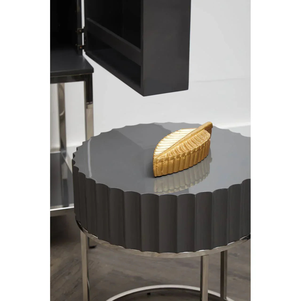 Round grey side table with ribbed edges and gold leaf ornament on glossy top