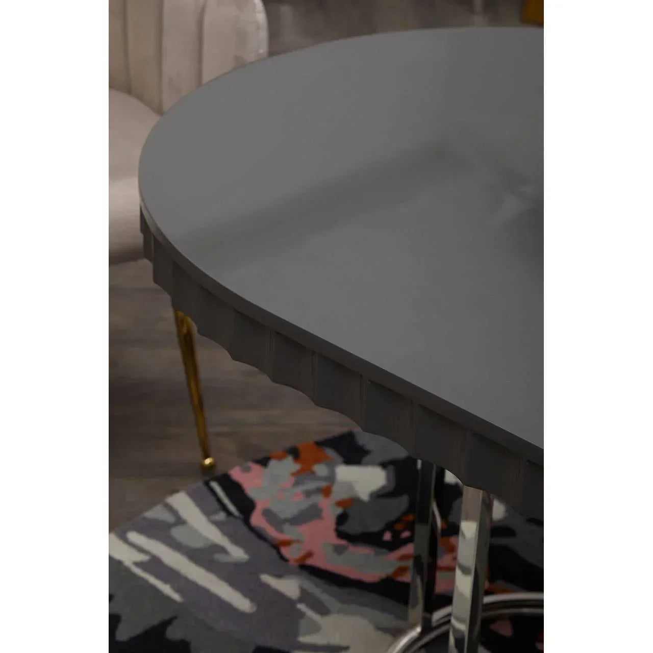 Round grey dining table with metallic legs beside upholstered chair on patterned rug