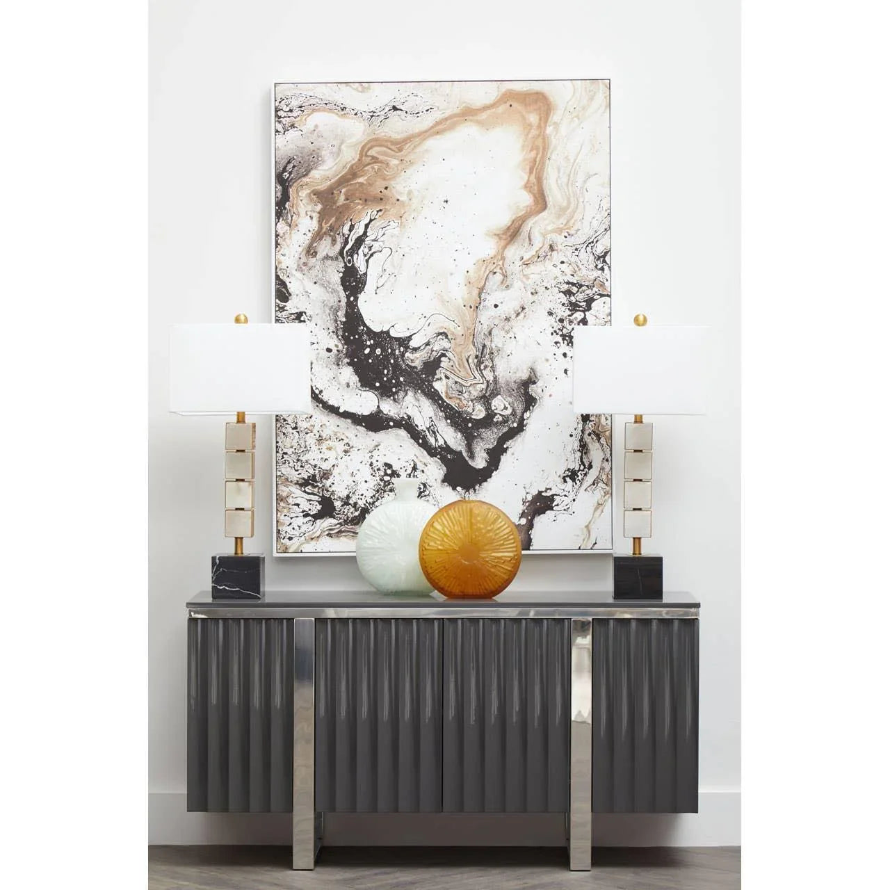 Grey sideboard with metallic legs, two table lamps, glass vases, and abstract wall art