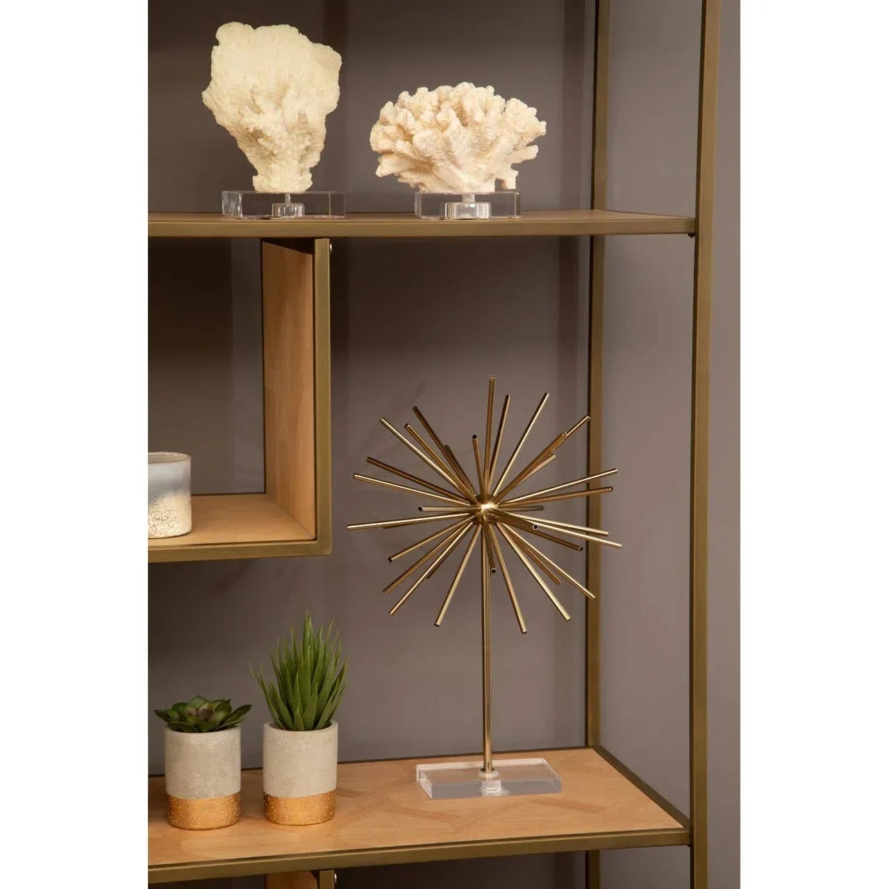 Gold metal decorative sculpture on wooden shelving unit with faux plants and coral accents