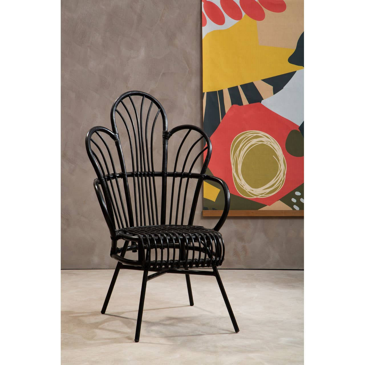 A stylish chair featuring a scalloped back design made of black natural rattan and supported by a black metal frame. The chair is positioned on a light-colored floor, with a colorful abstract wall art piece visible in the background