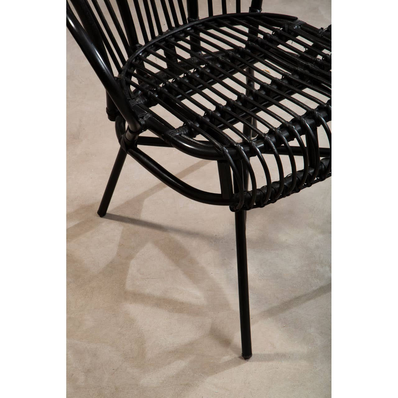 A black metal chair with a scalloped back design, featuring natural rattan weaving on the seat and backrest. The chair has slender legs and is positioned on a light-colored floor, casting a subtle shadow