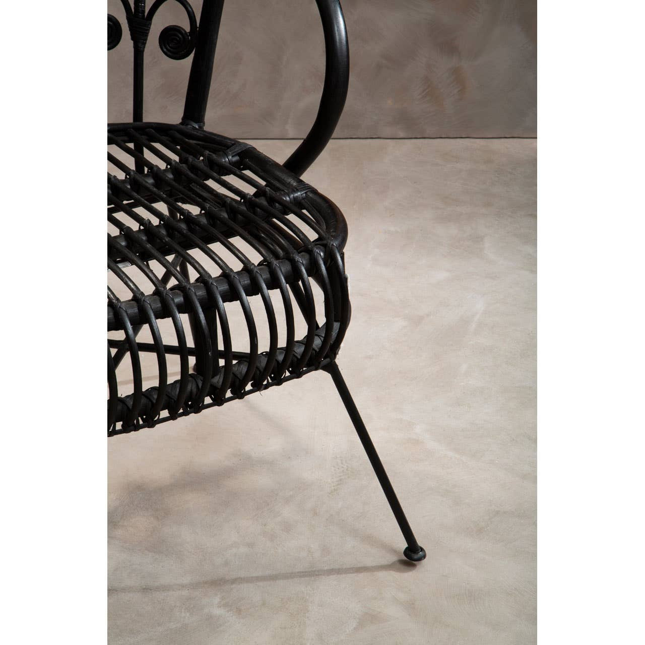 Black natural rattan chair with a scalloped back design, featuring a woven seat and slender metal legs, set against a neutral textured background