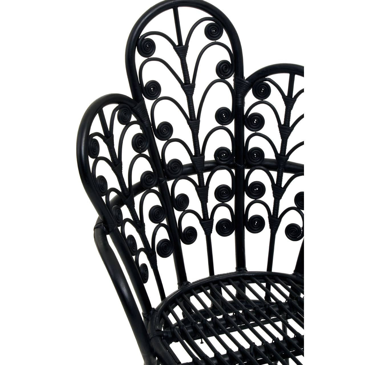 Scalloped back of a black rattan chair featuring intricate leaf and vine patterns, showcasing a blend of elegance and natural design. The chair's structure highlights its woven texture and sturdy frame, suitable for home decor