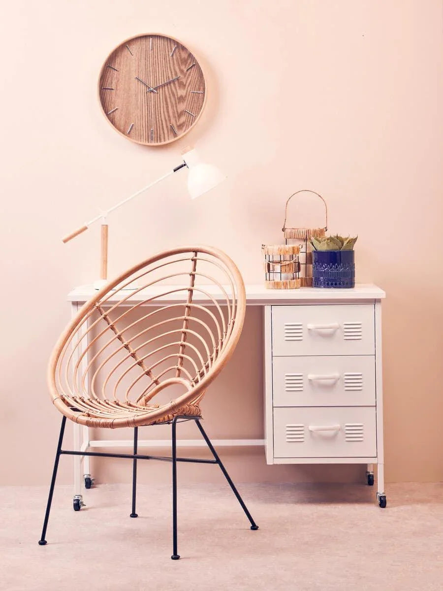 Rattan accent chair with black metal legs beside white desk and wooden wall clock