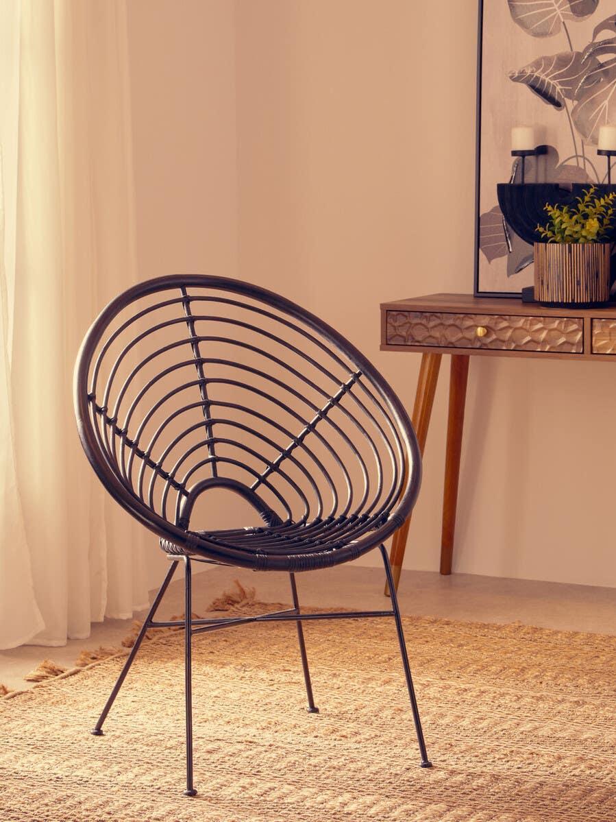 Black rattan accent chair with metal legs on woven rug in modern living room