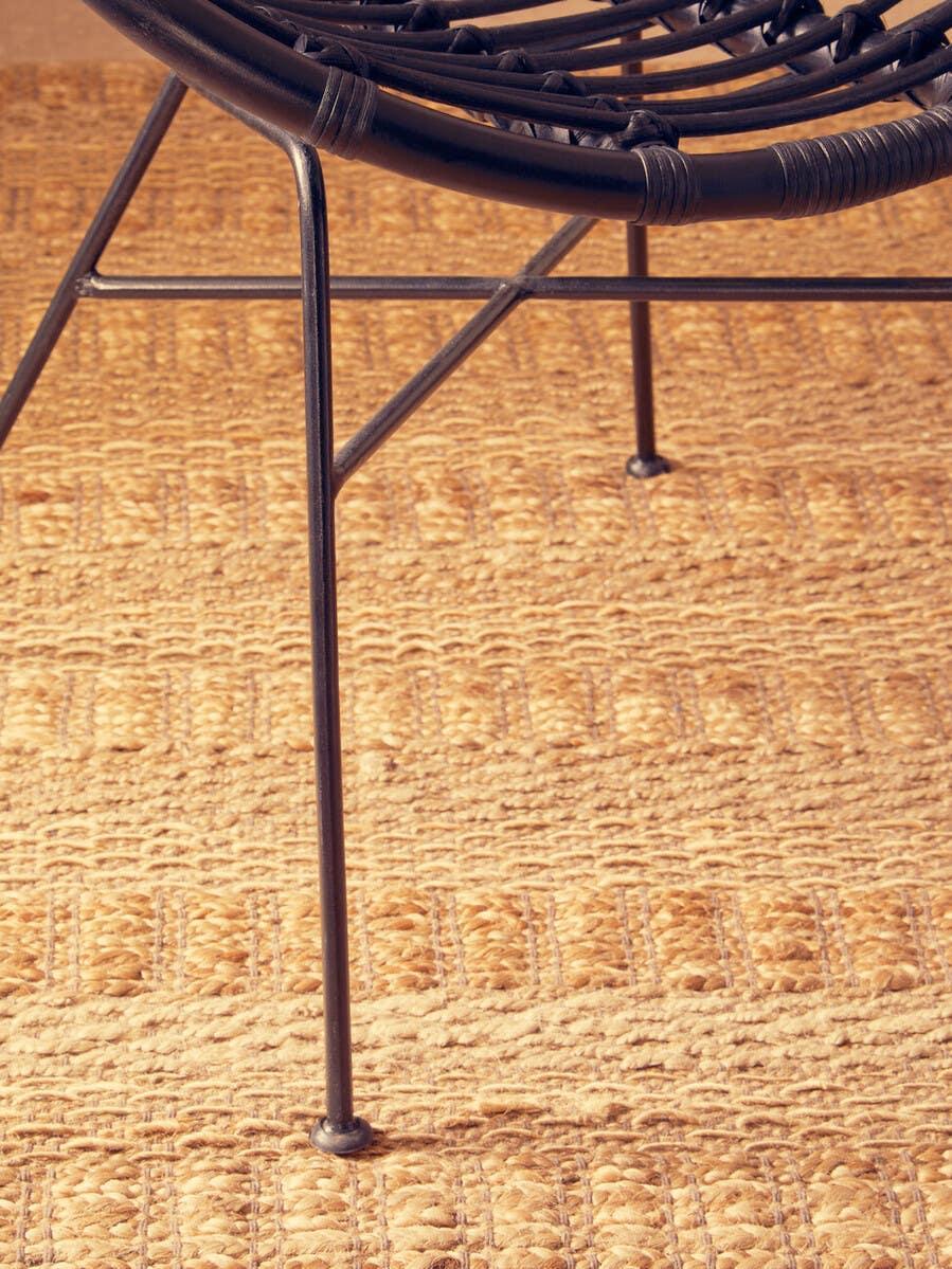 Black metal rattan chair leg on textured woven natural jute rug