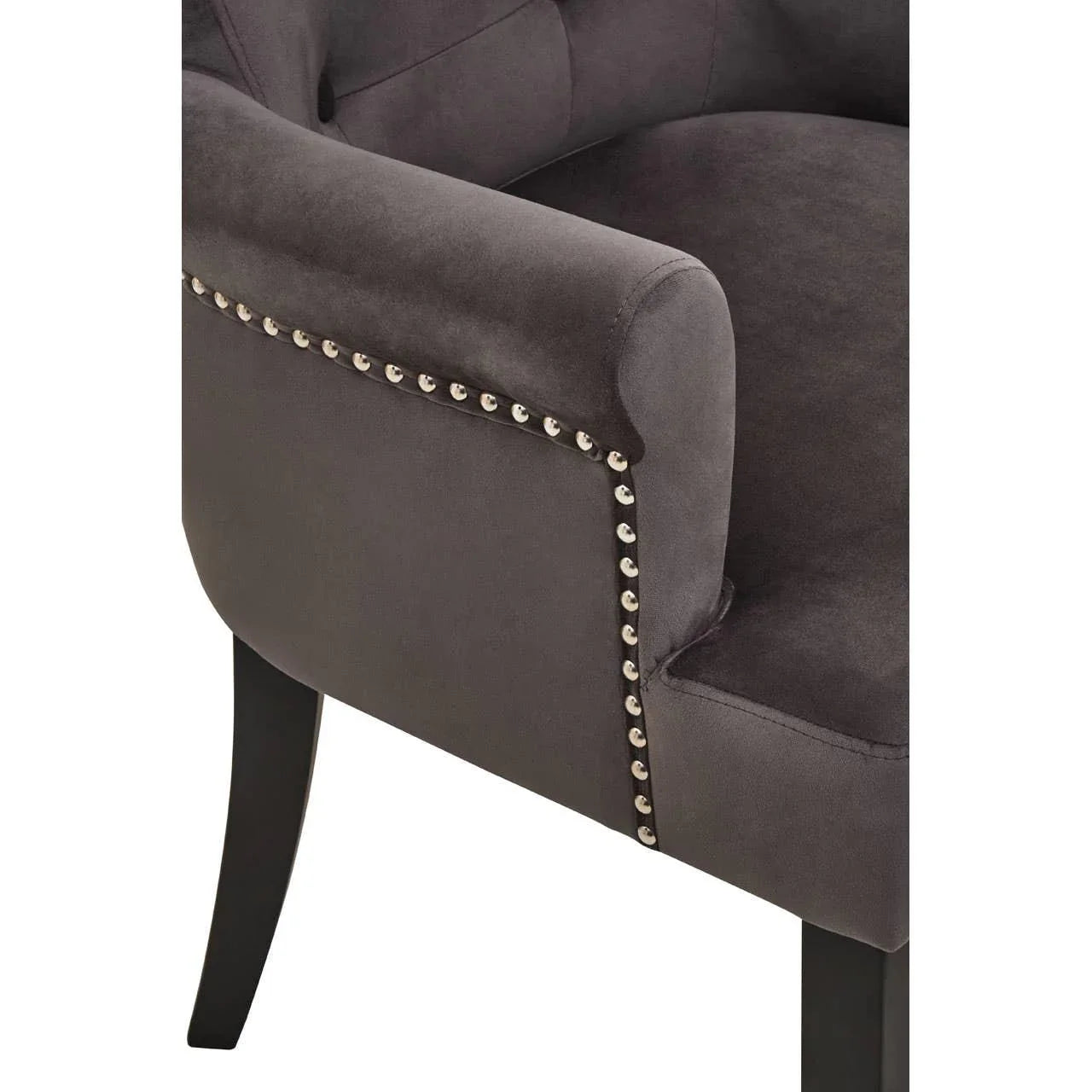 Grey velvet armchair with studded trim and black wooden legs, close-up view of armrest