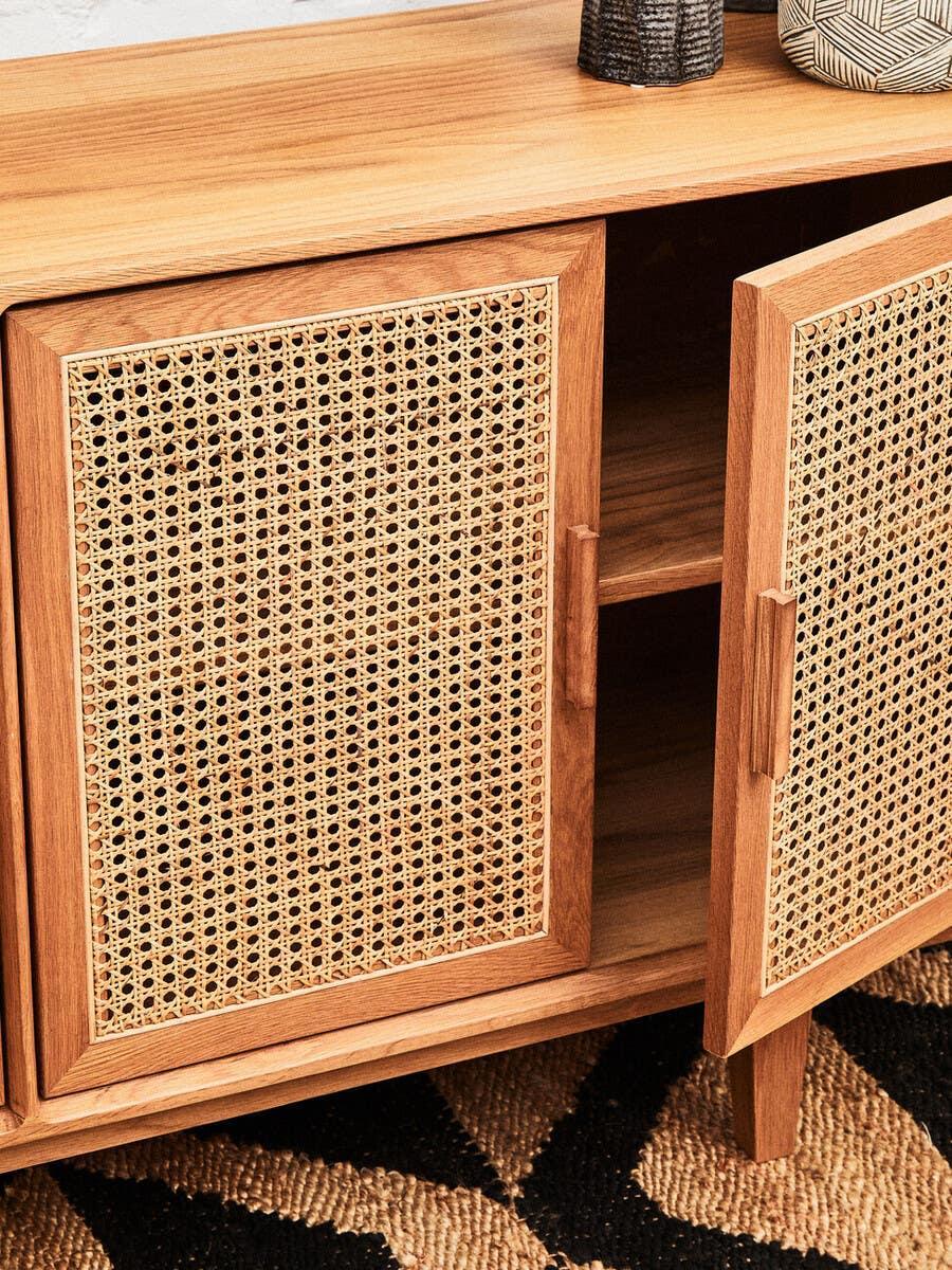 Wooden sideboard with woven rattan doors, one open to show interior shelf, on patterned rug