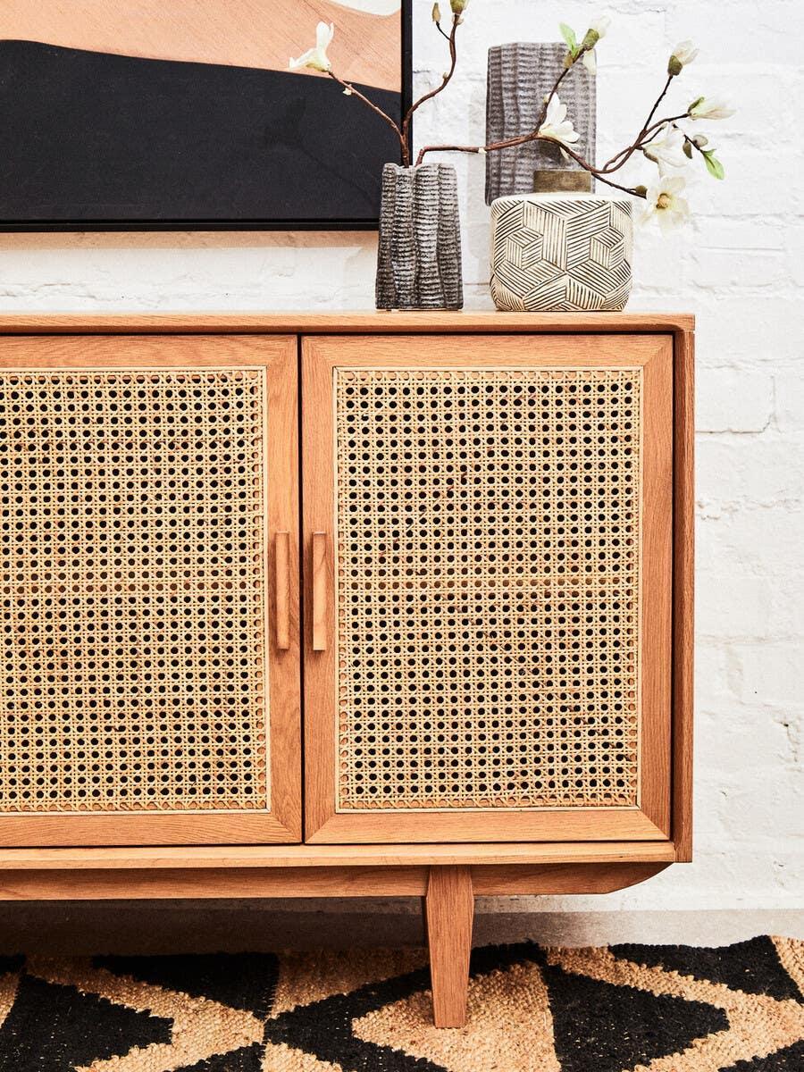 Oak sideboard with woven cane doors, decorative vases, and modern wall art above
