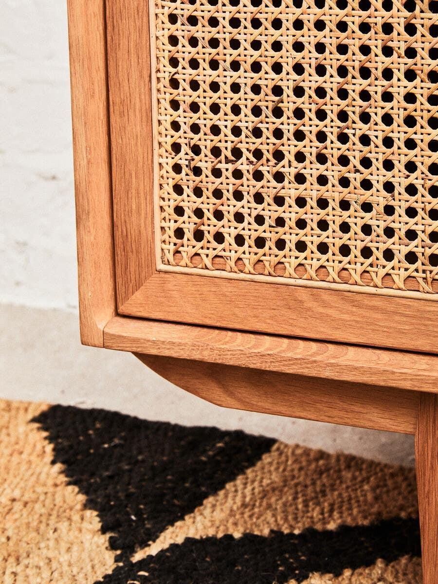 Close-up of wooden sideboard with rattan panel and geometric pattern rug
