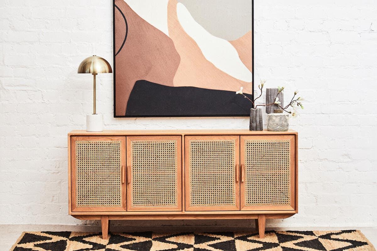 Rattan sideboard with wood frame, decorative lamp, vases, and abstract art on wall