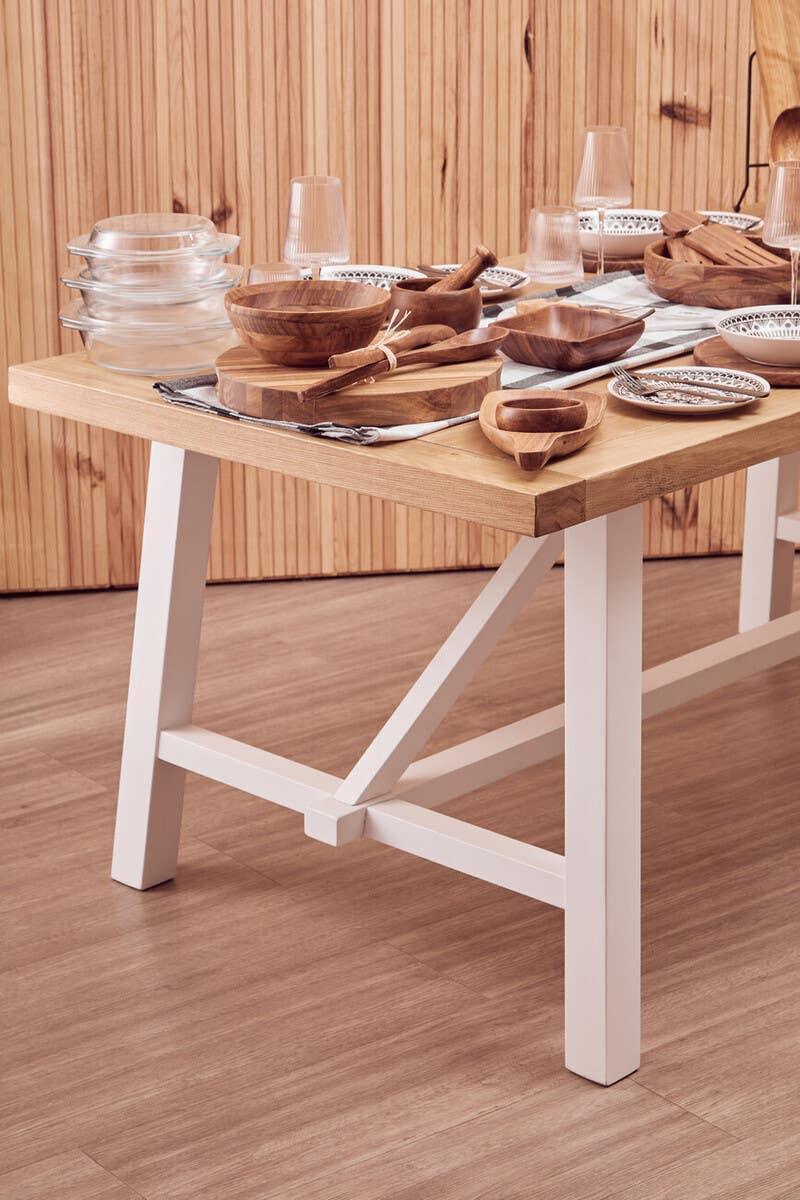 Wooden dining table with white legs set with bowls, plates, utensils and glassware