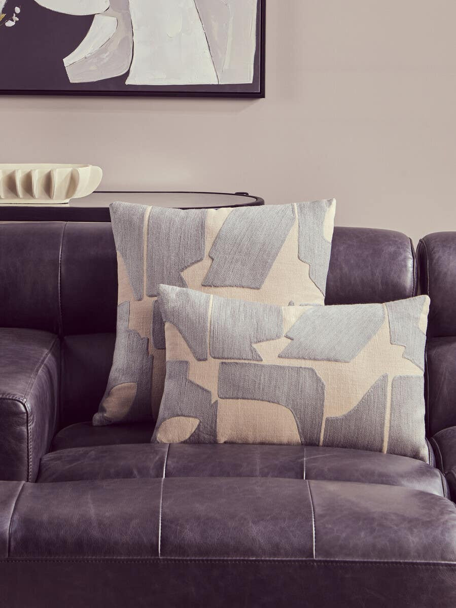 Left arm leather modular chaise sofa in antique black with two decorative pillows featuring a geometric pattern in beige and gray, set against a neutral wall with a framed artwork in the background