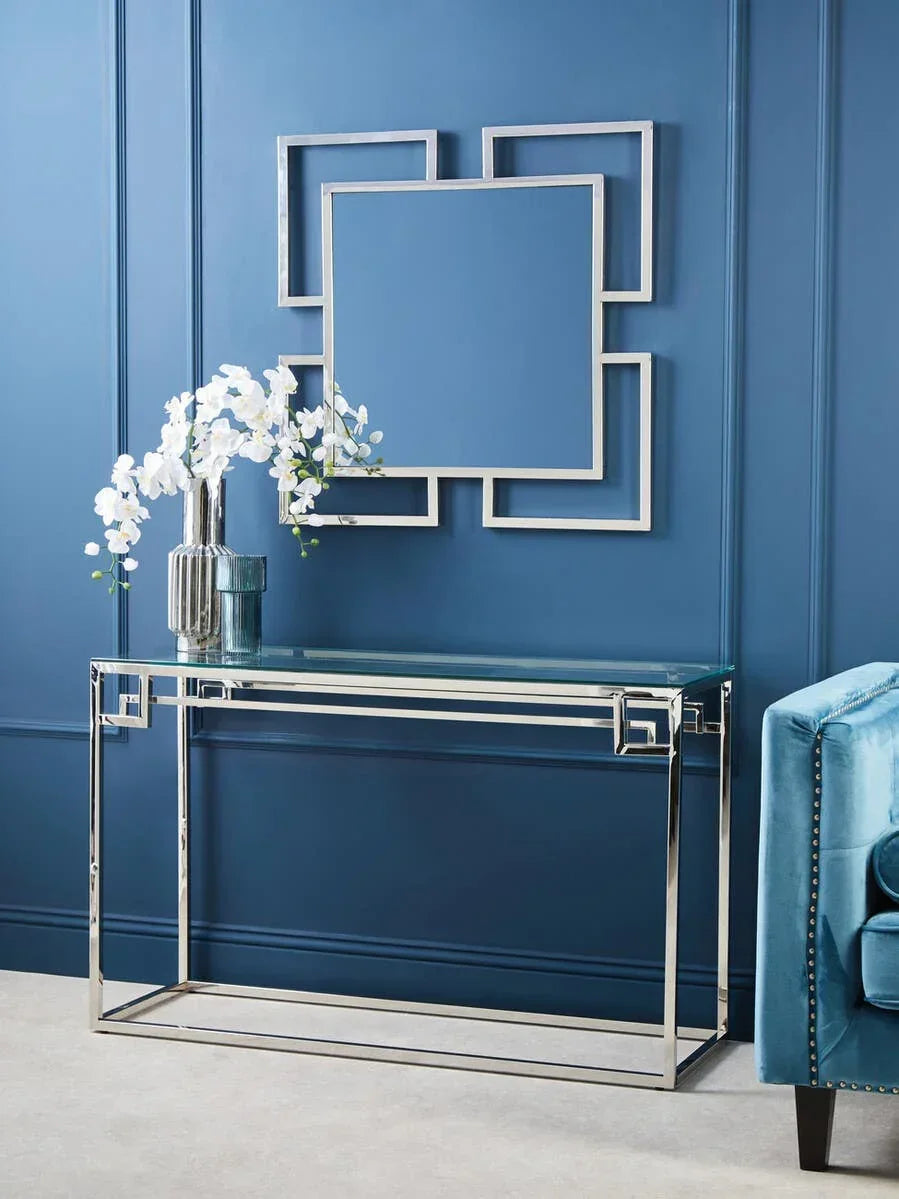 Glass console table with chrome frame and decorative chrome mirror against blue wall