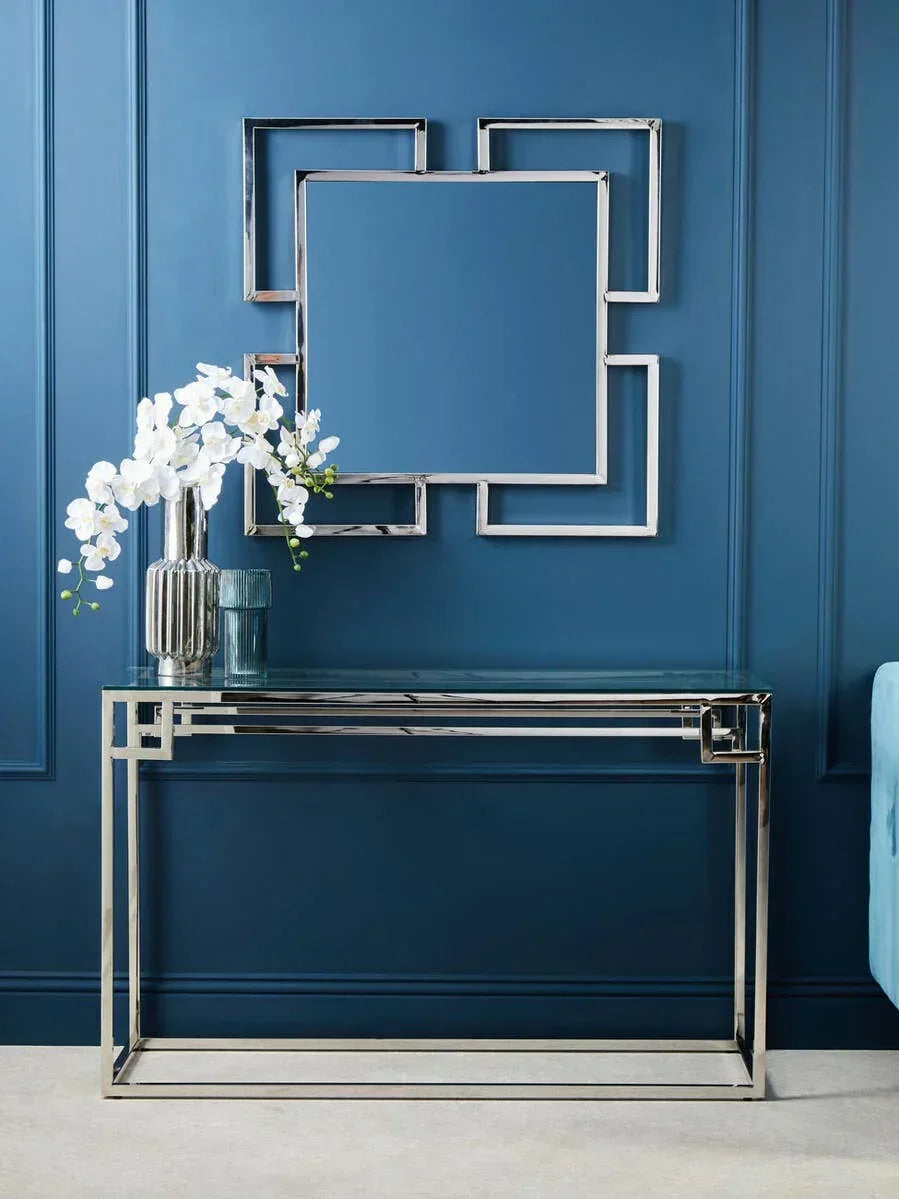 Chrome console table with glass top and matching geometric wall mirror against blue wall