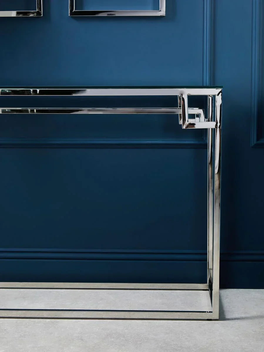 Chrome and glass console table with modern geometric frame against blue wall