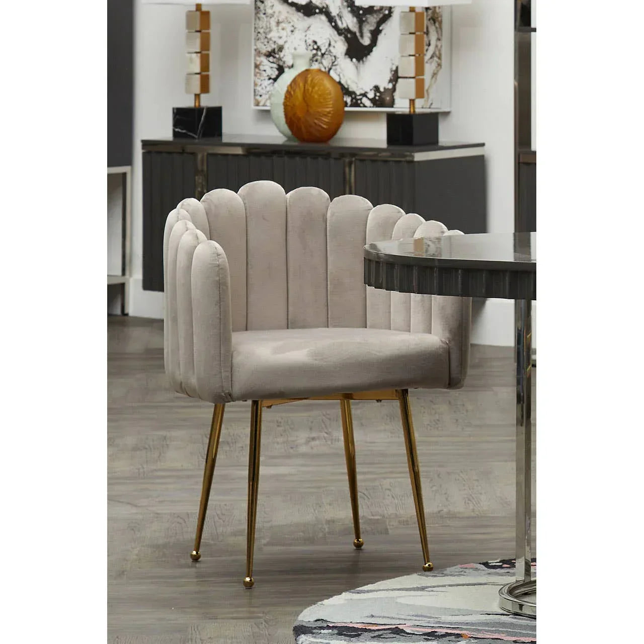 Beige velvet accent chair with scalloped backrest and gold metal legs beside round dining table