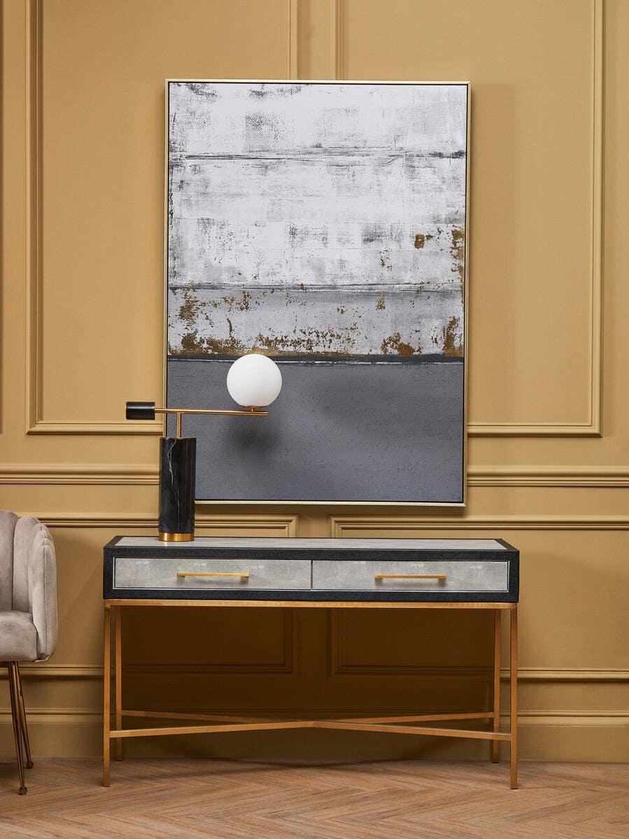 Contemporary console table with gold legs, grey drawers, and modern lamp against tan wall