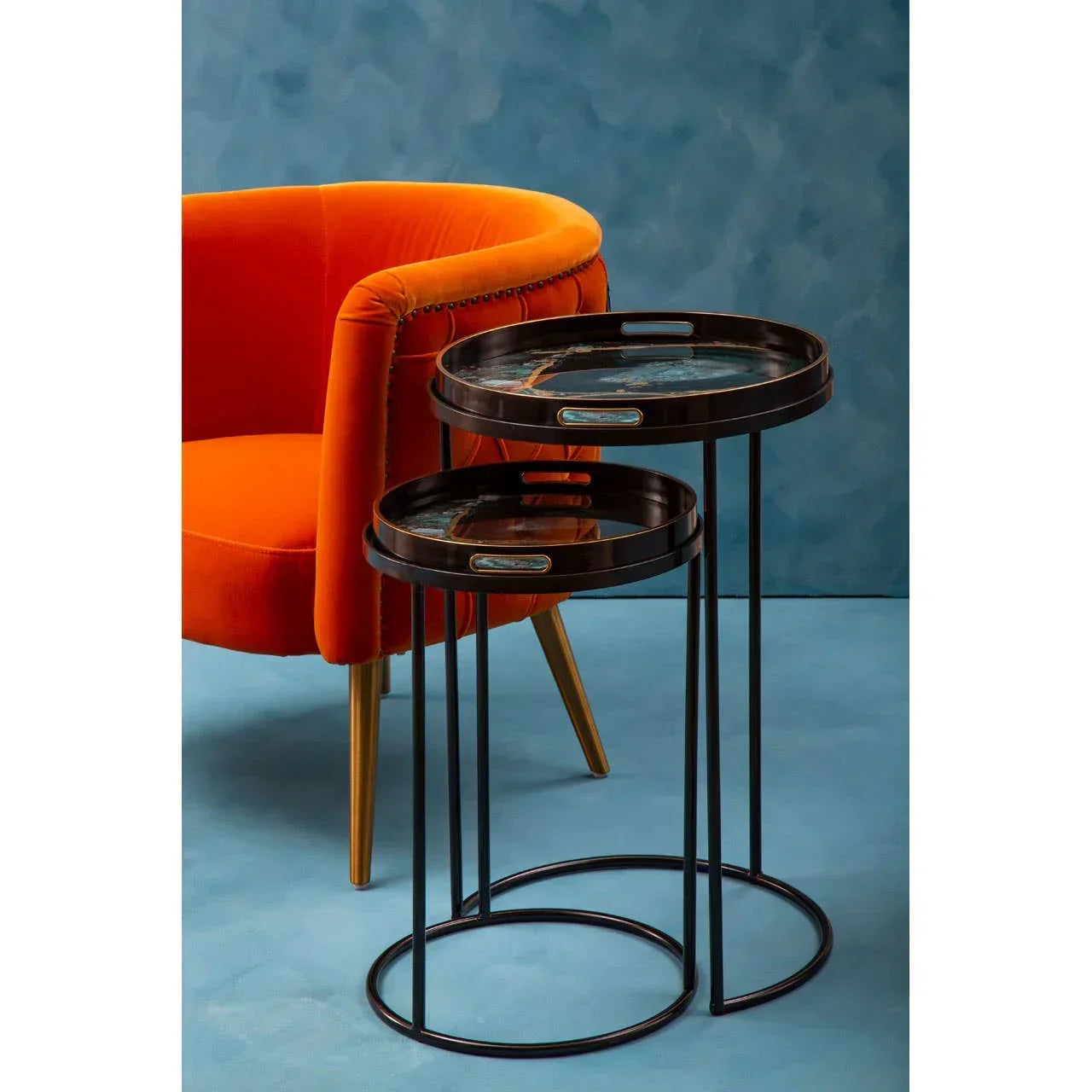 Round nesting side tables with black metal frames beside an orange velvet accent chair