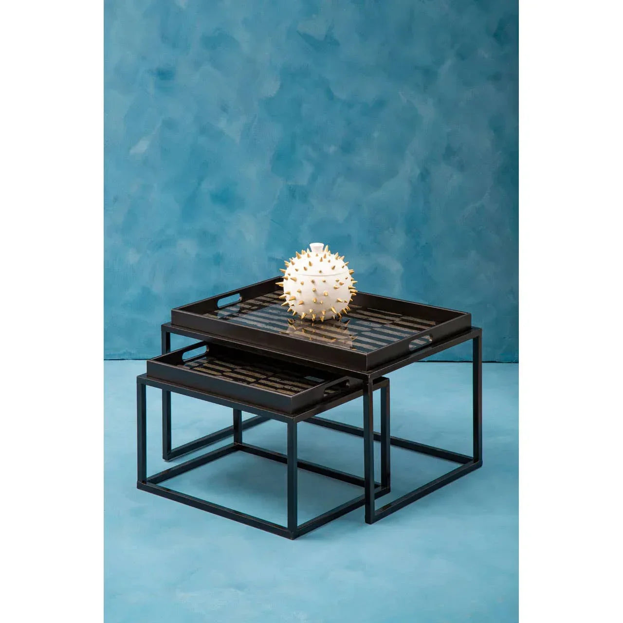 Set of black metal nesting coffee tables with decorative vase on blue background