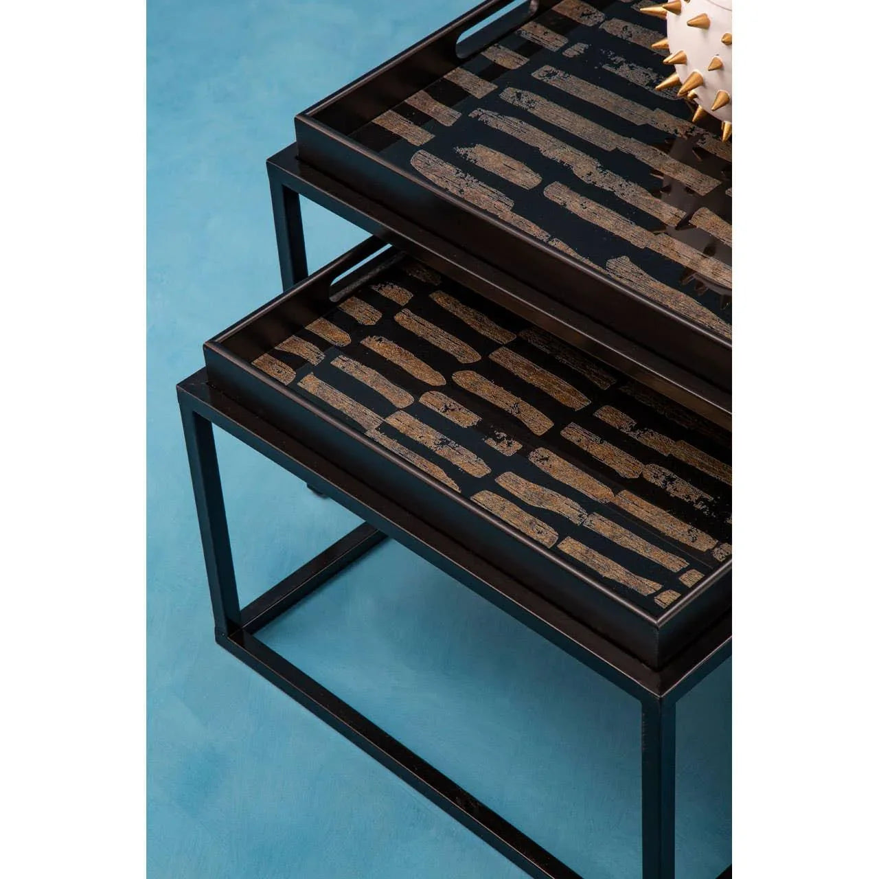 Set of two black metal nesting tables with patterned tops on a blue floor