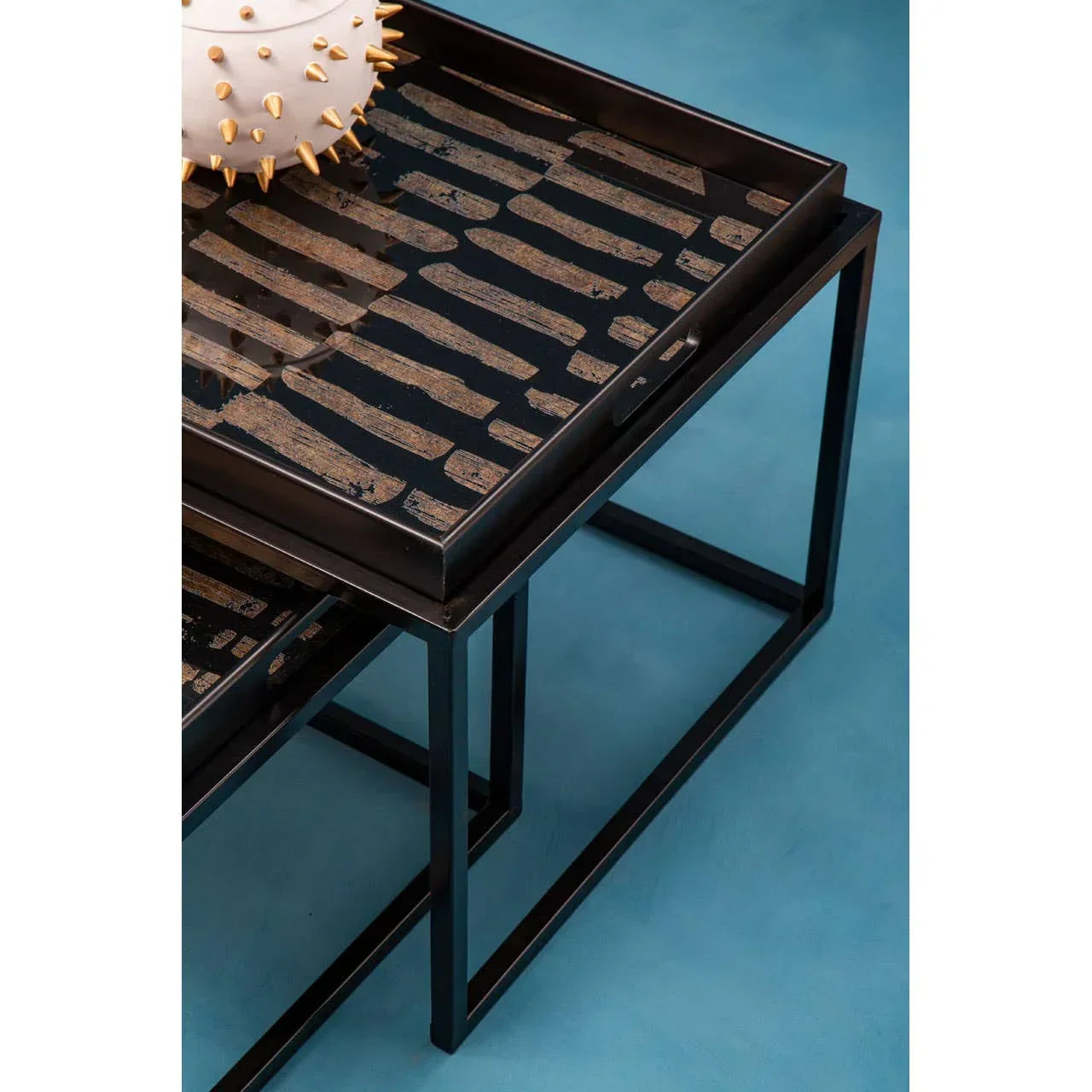Black metal nesting tables with patterned glass tops on a blue floor