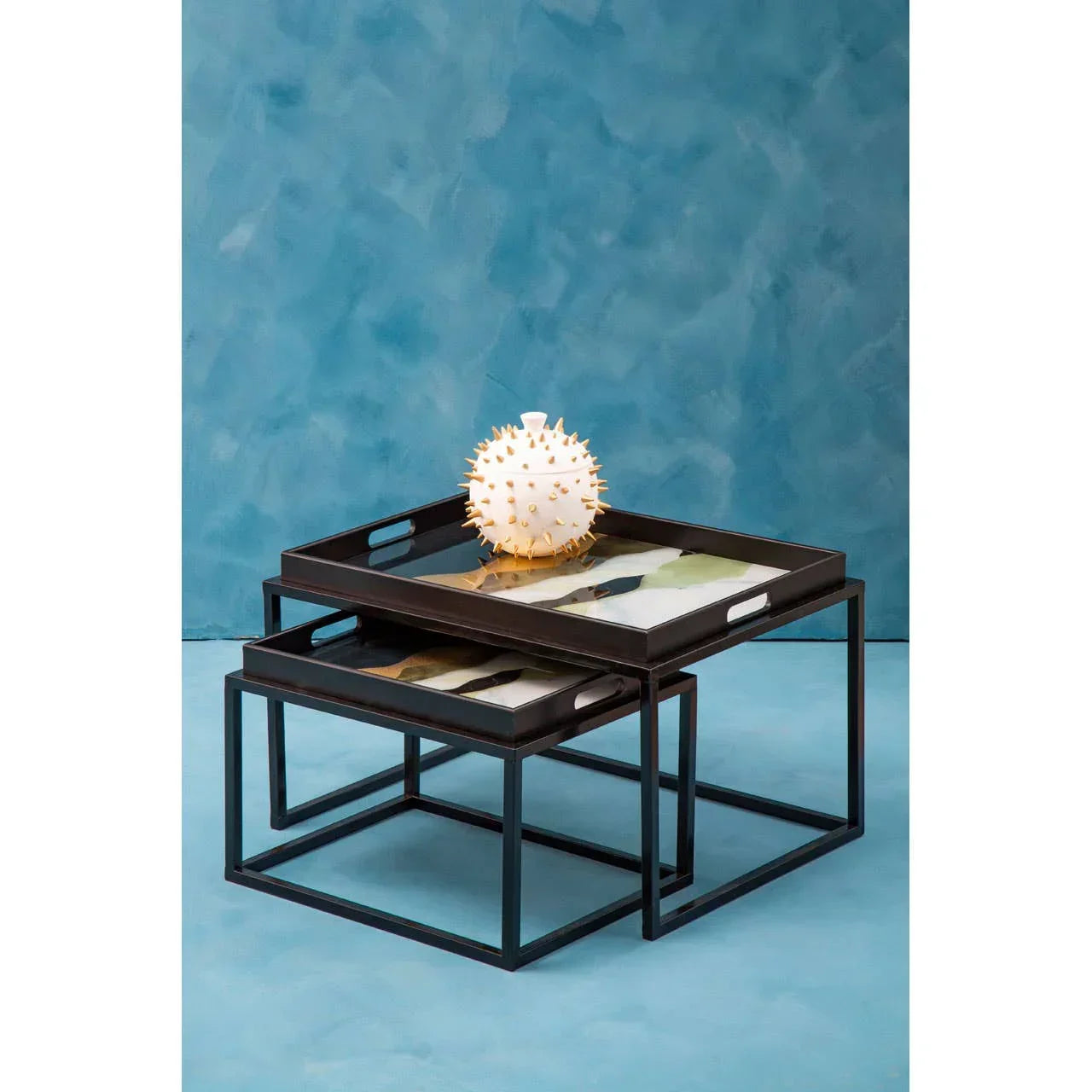 Black metal nesting coffee tables with tray tops and geometric base on blue background