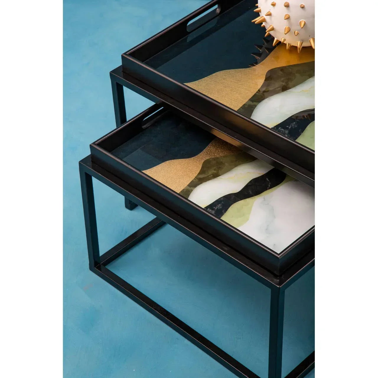 Black metal nesting tables with multicoloured abstract glass tops on blue floor