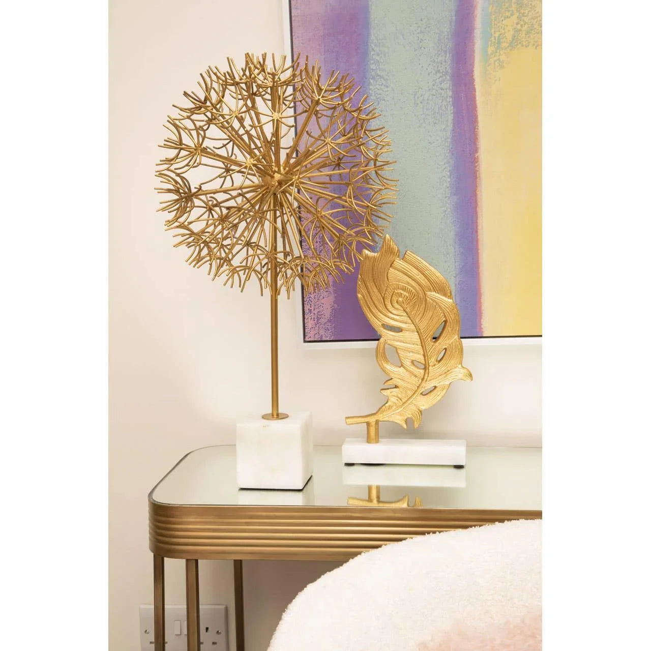 Gold metal dandelion and leaf ornaments on marble bases atop mirrored console table